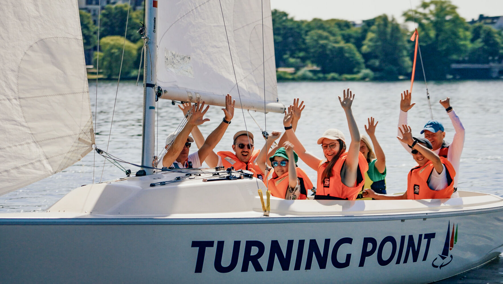 Menschen sitzen in einem Segelboot mit der Aufschrift Turning Point. Sie winken.