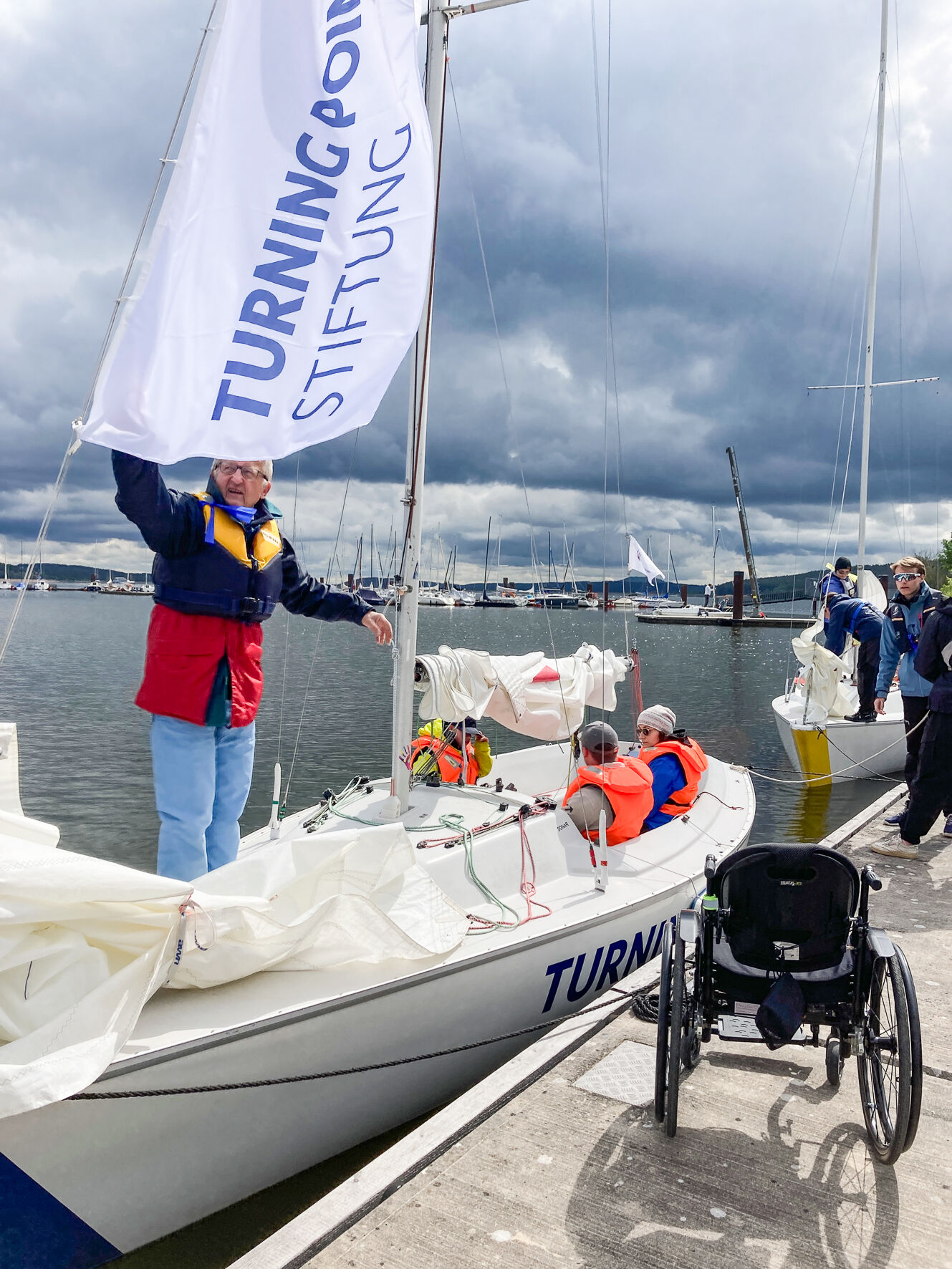 Eine Sonar liegt am Steg. Davor steht ein Rollstuhl. Ein Trainer nimmt die Flagge der Stiftung herunter.