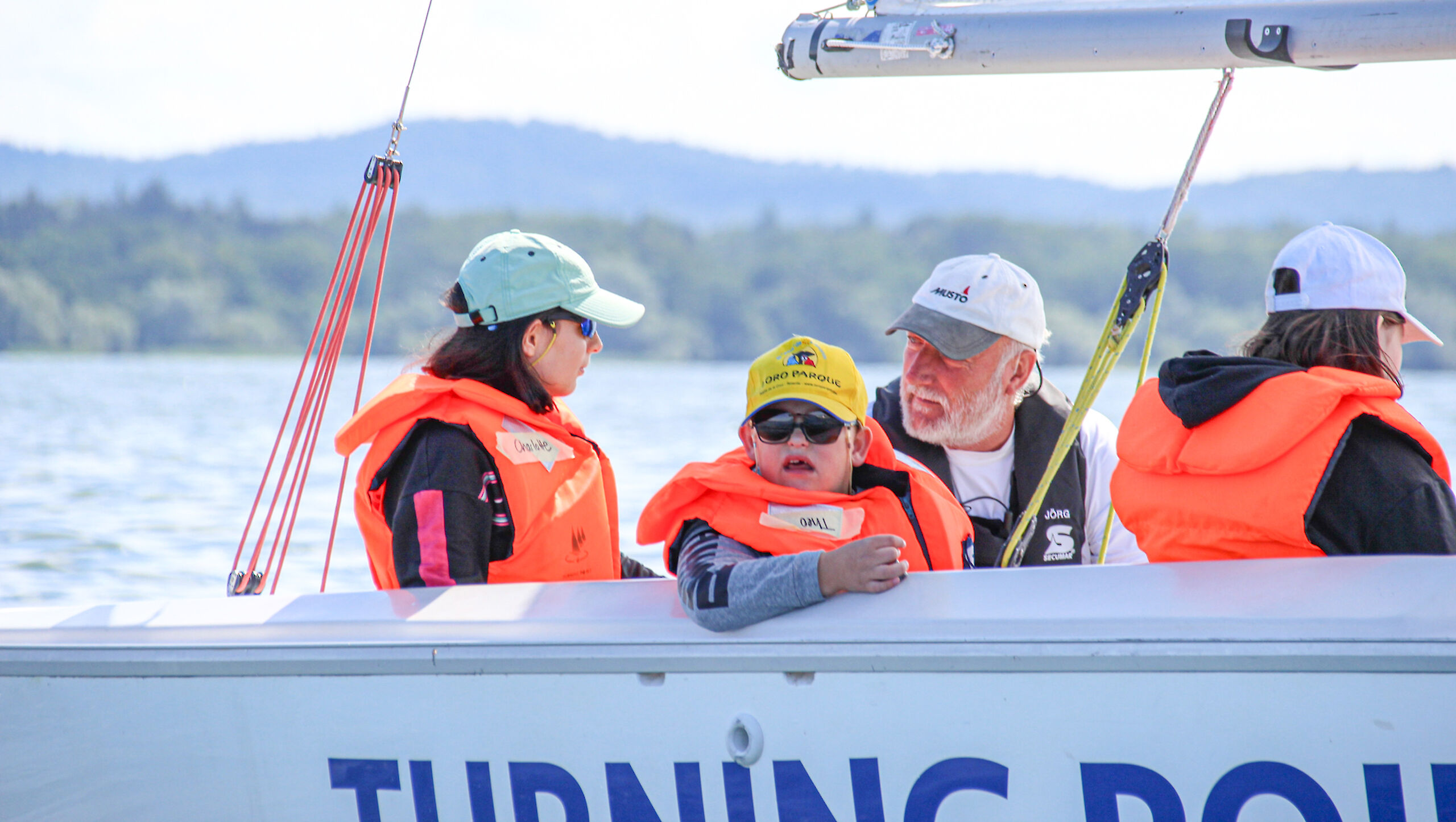 Vier Menschen in Schwimmwesten sitzen auf einem Segelboot