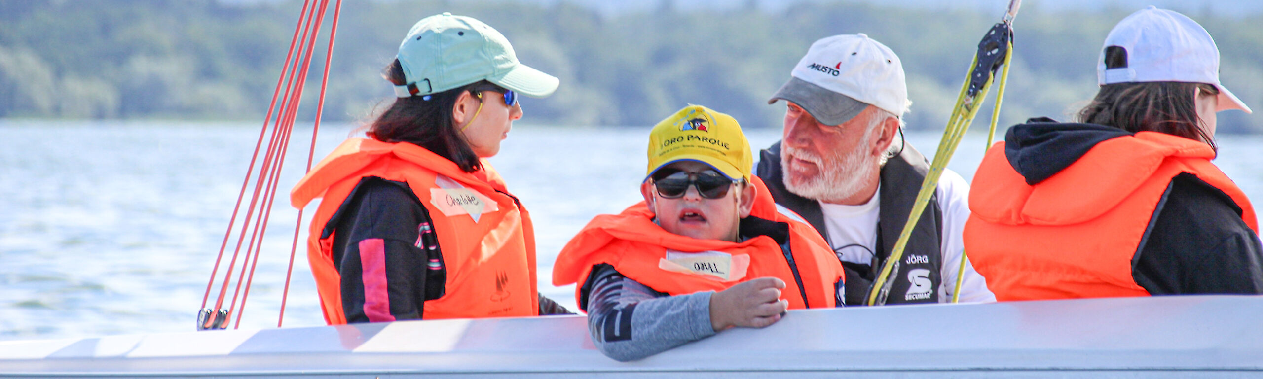 Vier Menschen in Schwimmwesten sitzen auf einem Segelboot