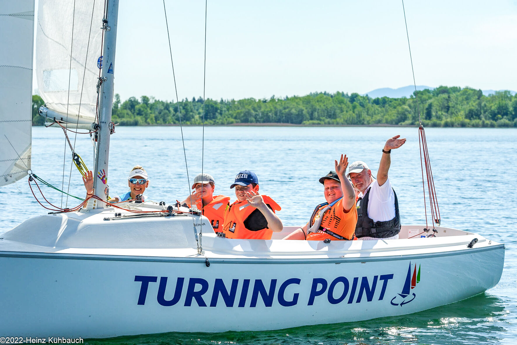 People sitting in a sailing boat. They are laughing and waving.