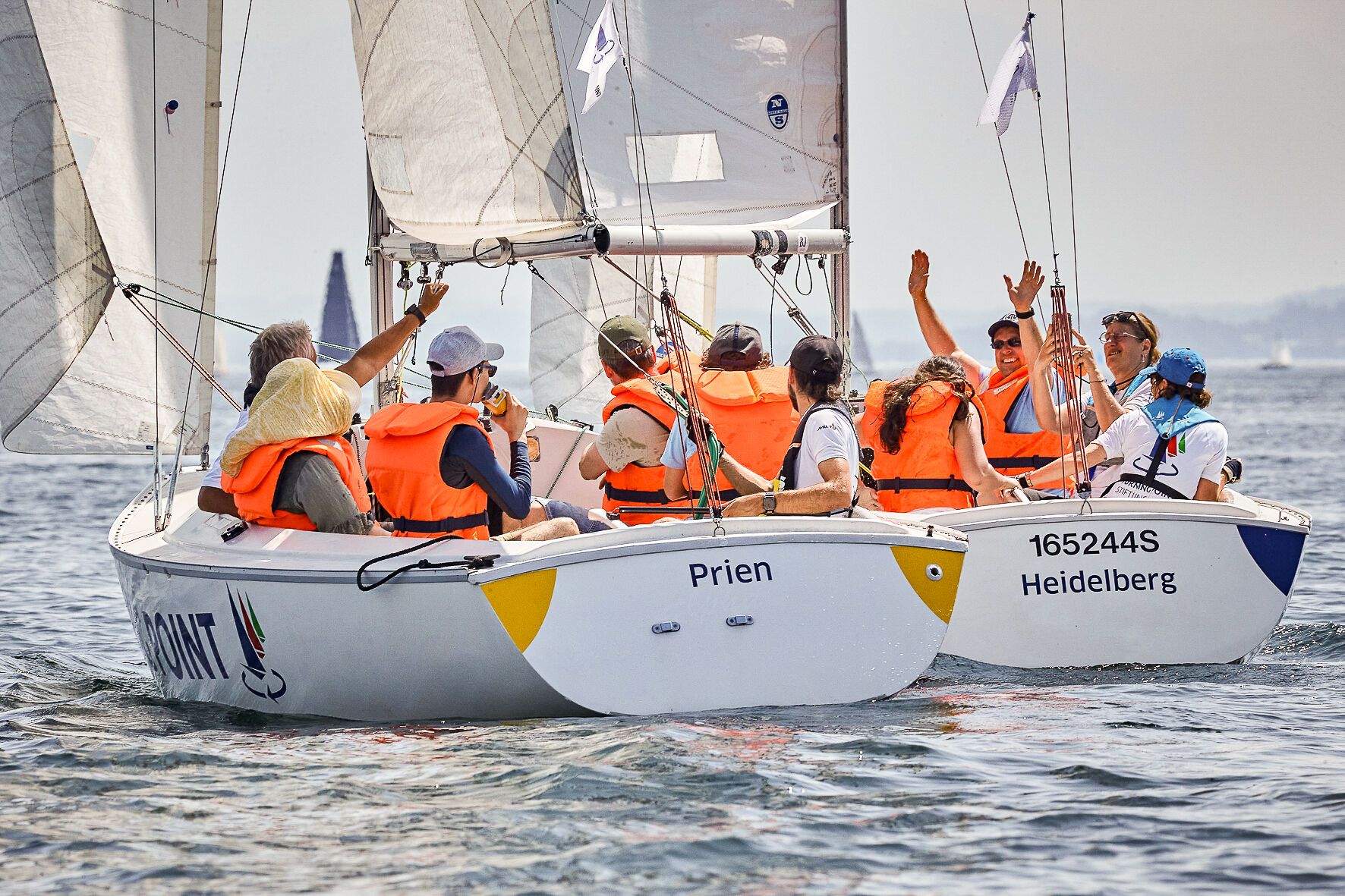 Mehrere Menschen sitzen in zwei Sonar Booten. Einige winken. Alle haben Rettungswesten an.